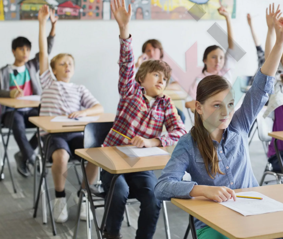 A group of children raising their hands in a classroom Description automatically generated